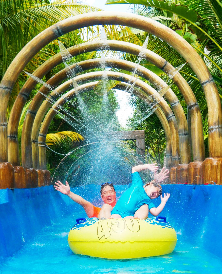 Two riders on a yellow tube passing under bamboo arches spraying water.