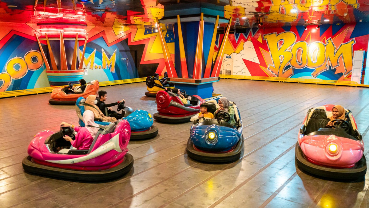 Riders in dodgem cars on a polished floor in front of a comic-book style painted wall.