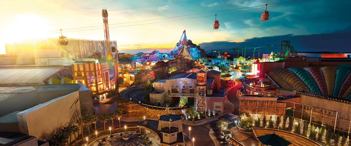 The theme park at dusk from above, with cable cars crossing over the lit rides.