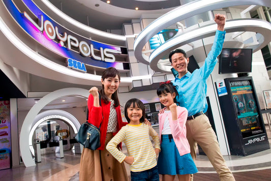 A family posing beneath the illuminated Joypolis Sega sign at the park entrance.