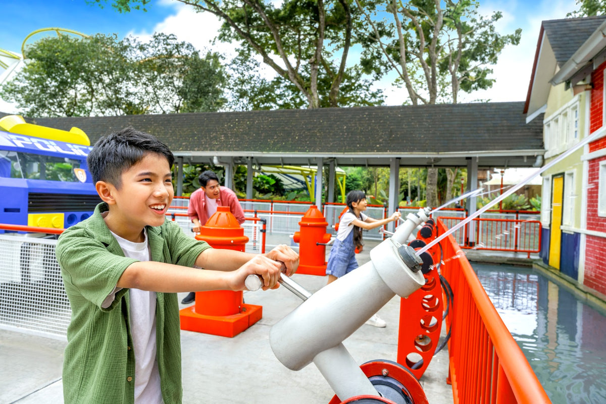 A boy aiming a water cannon across a pool, with other visitors at cannons along the rail behind him.