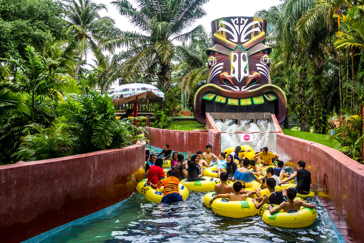 Visitors floating in yellow rings along a lazy river, passing a carved tiki mask in the greenery.