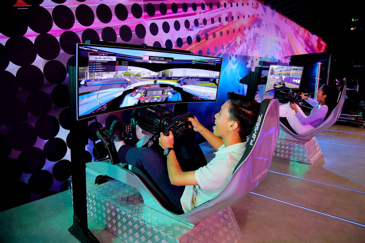 Two visitors racing in Formula One simulator seats with curved screens at Petrosains.