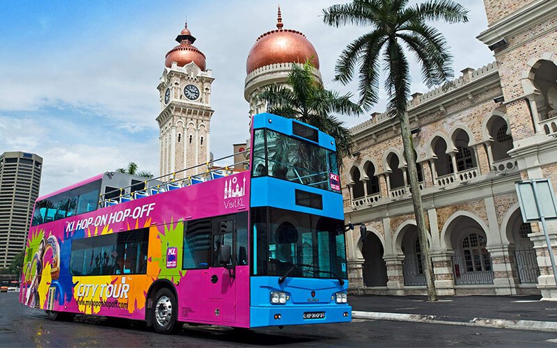 An open-top double-decker sightseeing bus outside the Sultan Abdul Samad Building.