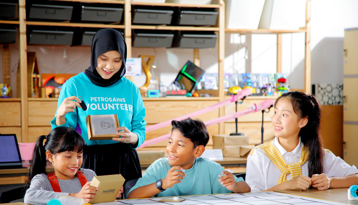 A Petrosains volunteer running a hands-on activity with three children at a workbench.