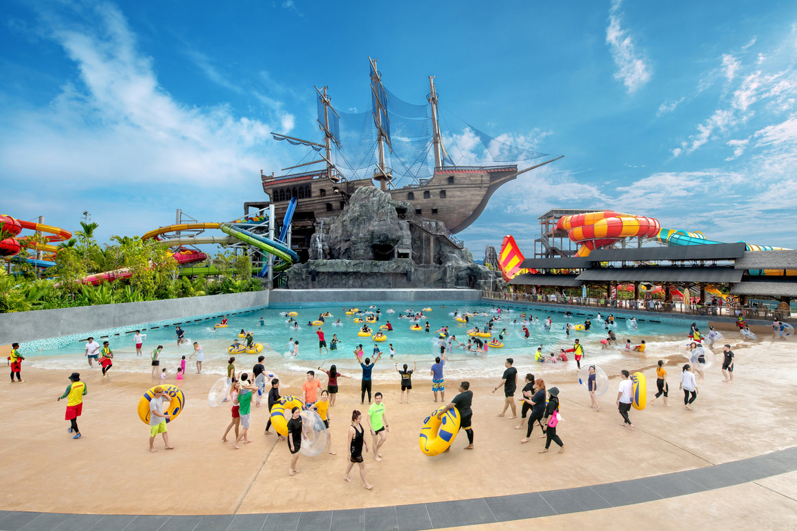 Crowds on the sand beach beside the wave pool, the pirate ship behind.