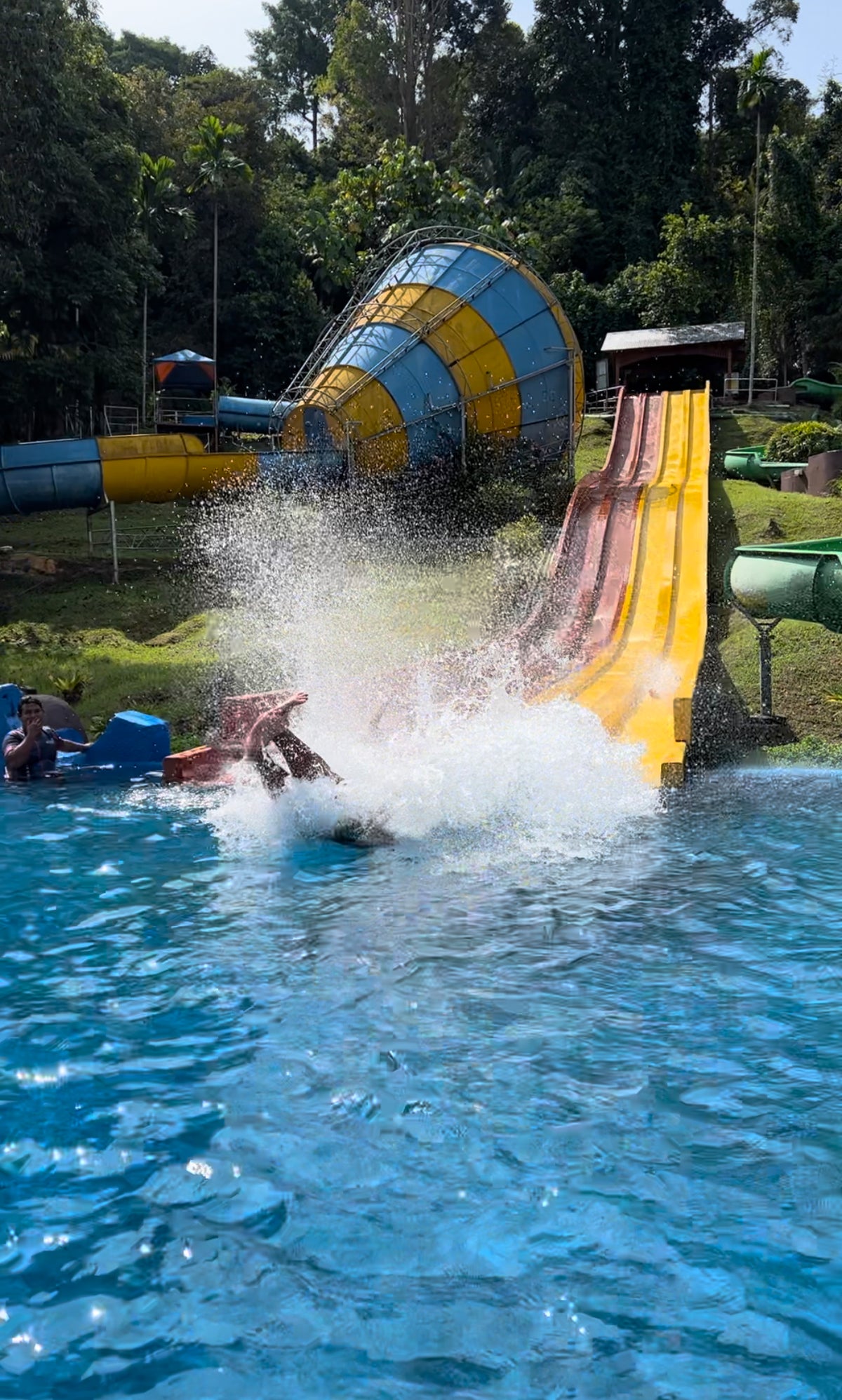 A rider hitting the splash pool at the bottom of a steep red and yellow racer slide.