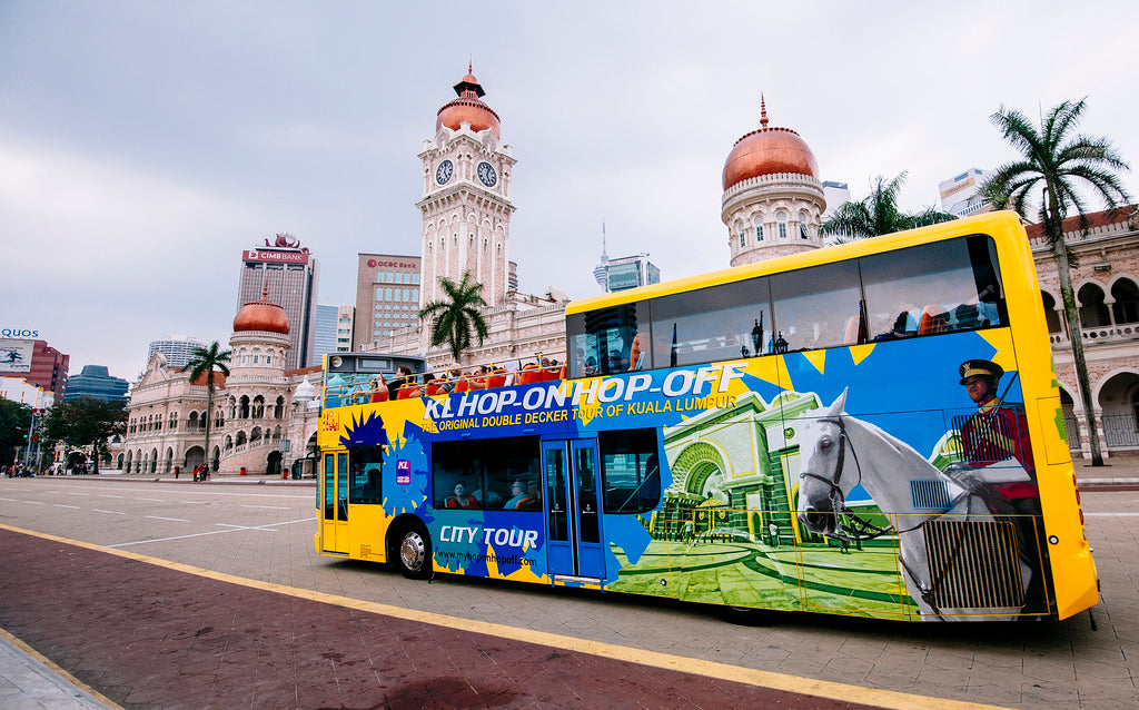A yellow and blue double-decker tour bus passing the Sultan Abdul Samad Building.