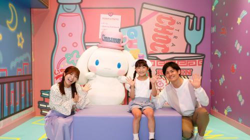 A family sitting with a giant Cinnamoroll soft toy in a pastel themed room