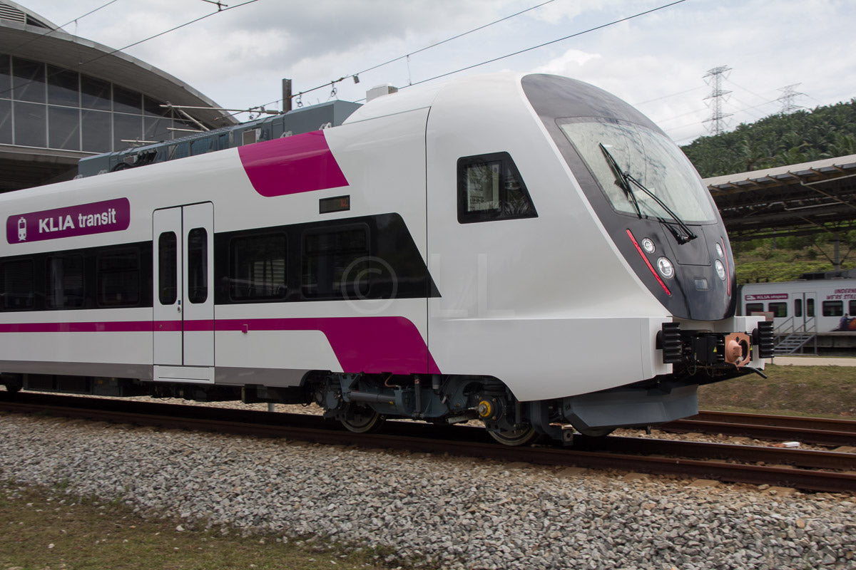 A KLIA Transit train in magenta and white livery stopped alongside a platform.
