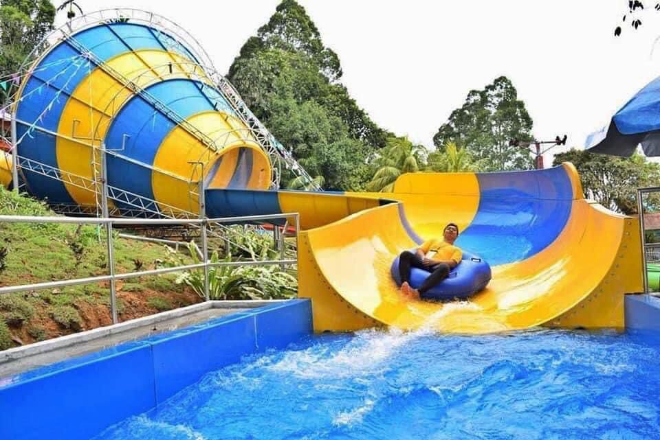 A rider on a yellow tube sliding down a wide curved chute beside the funnel slide.