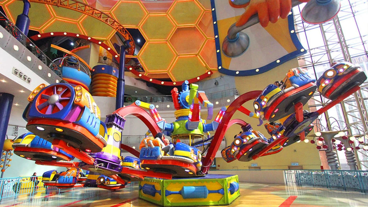 A brightly coloured spinning ride inside the indoor theme park, under a honeycomb ceiling.