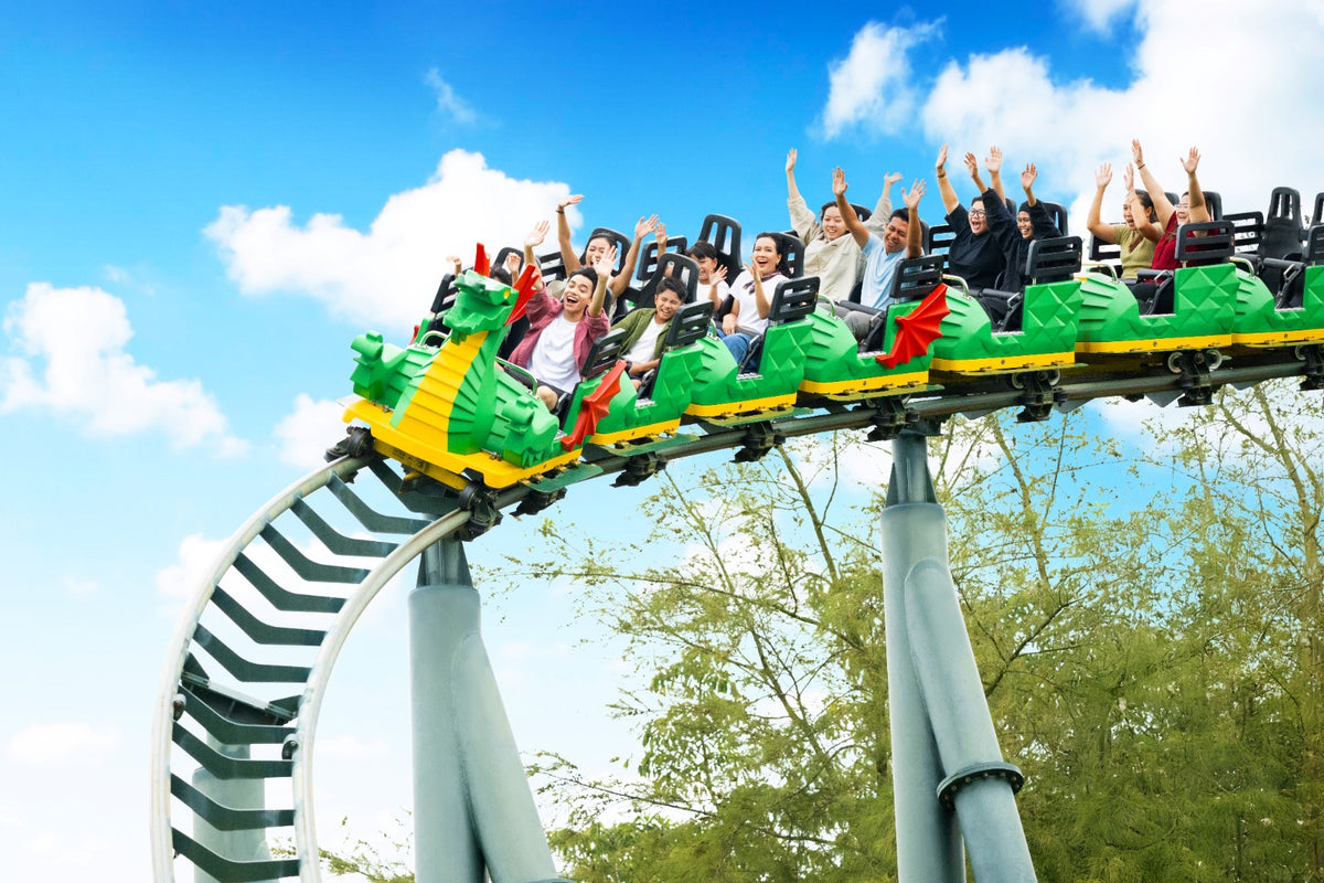 The green dragon-fronted roller coaster train running along the track, every rider with their hands up.