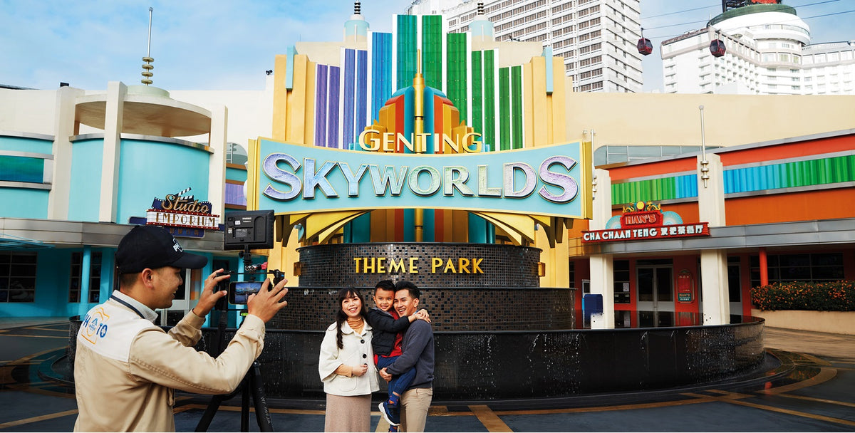 A photographer taking a couple's picture in front of the Genting SkyWorlds theme park sign.