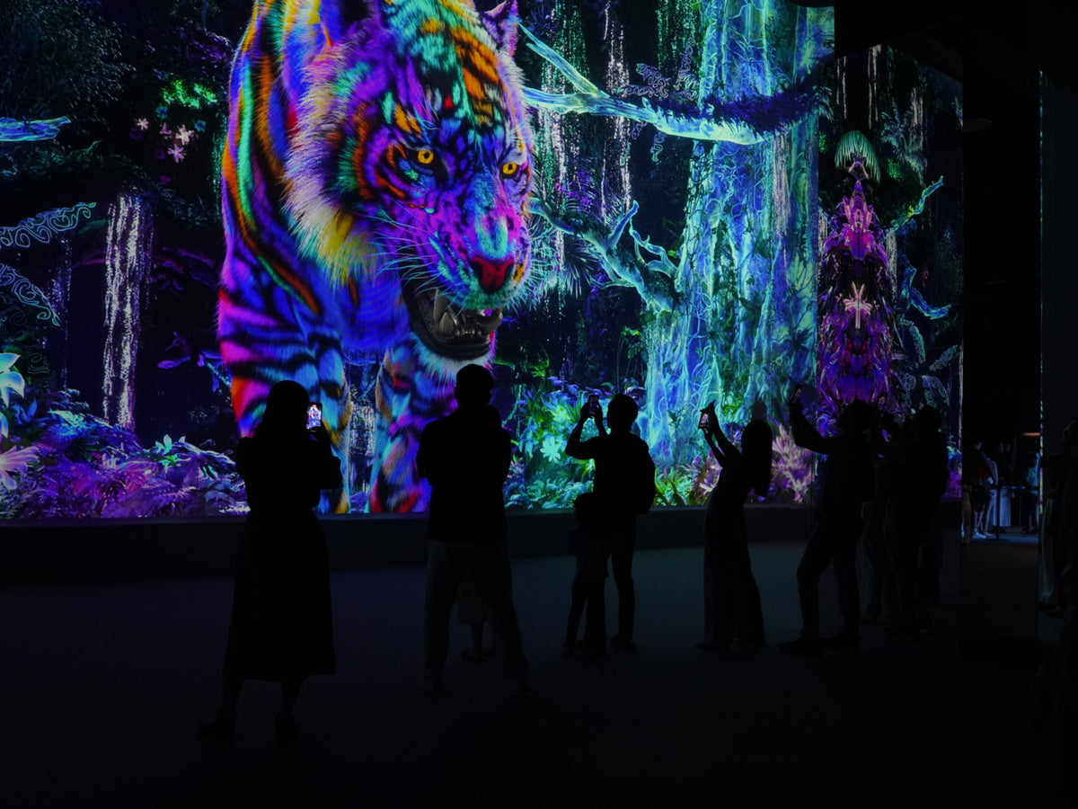 Visitors reaching towards a wall-sized projection of a tiger in neon colours.