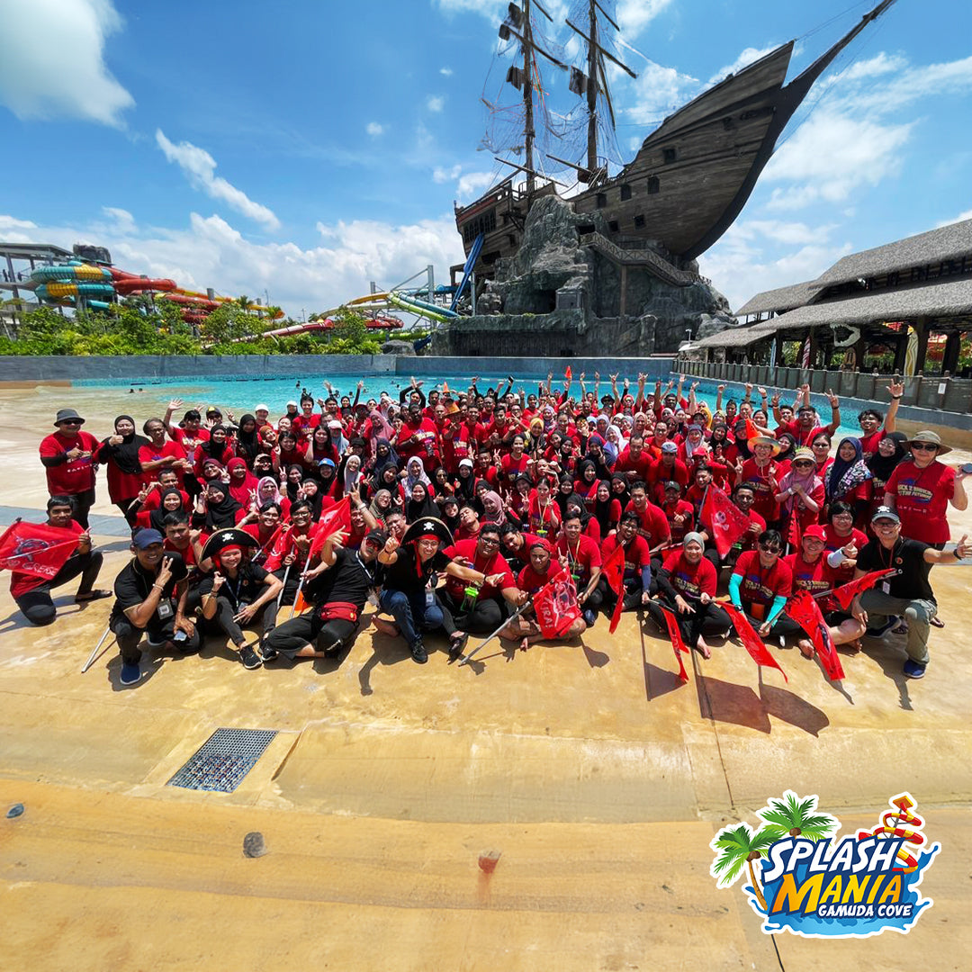 A large group in red shirts posed by the wave pool holding flags.