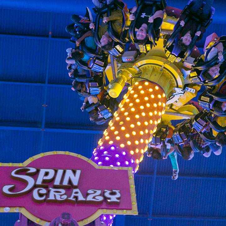 The Spin Crazy ride tilted against the blue indoor ceiling, seats empty.