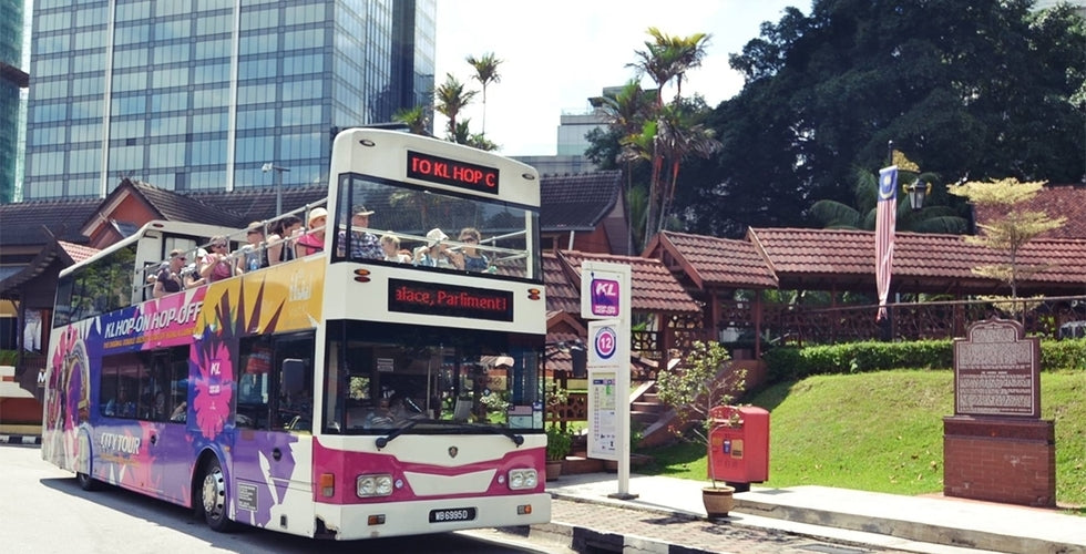 A pink and white open-top tour bus stopped beside a stop sign near a park.