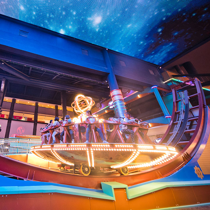 A spinning ride lit gold beneath the starfield ceiling of the indoor park.