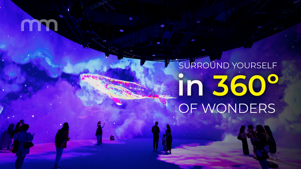 Visitors silhouetted in a projection hall, purple and pink imagery washing the walls and floor.