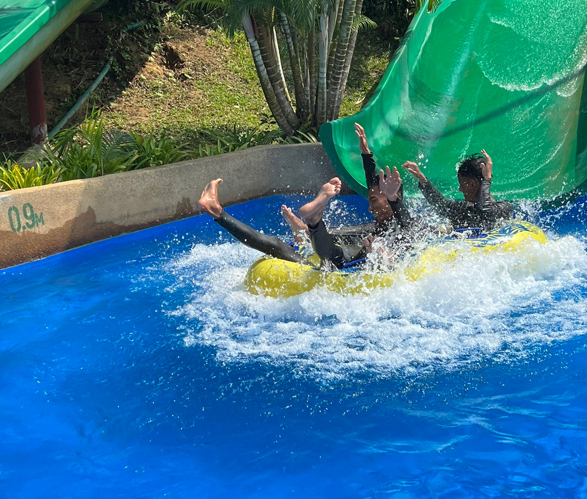 Three riders landing in the splash pool at the foot of an enclosed green slide.