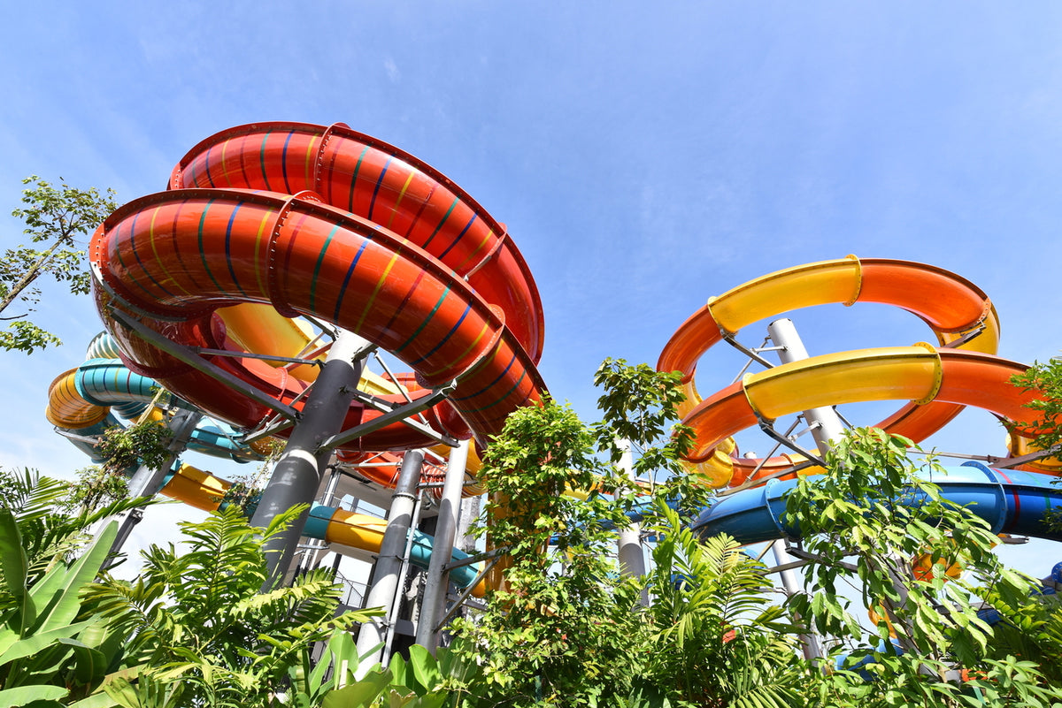 Looking up at red and orange spiral slides against a clear sky.
