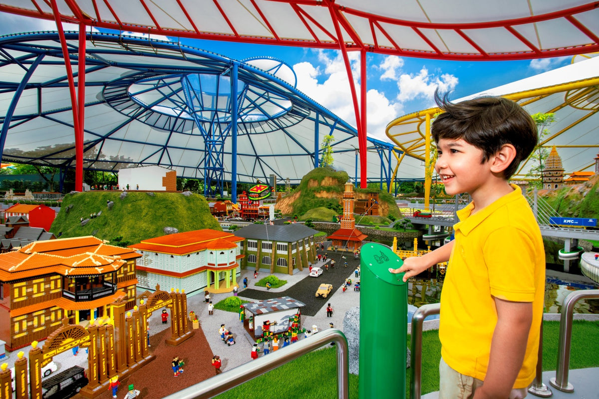 A boy at a viewing post above the MINILAND cityscape, looking across miniature buildings, roads and tiny vehicles.