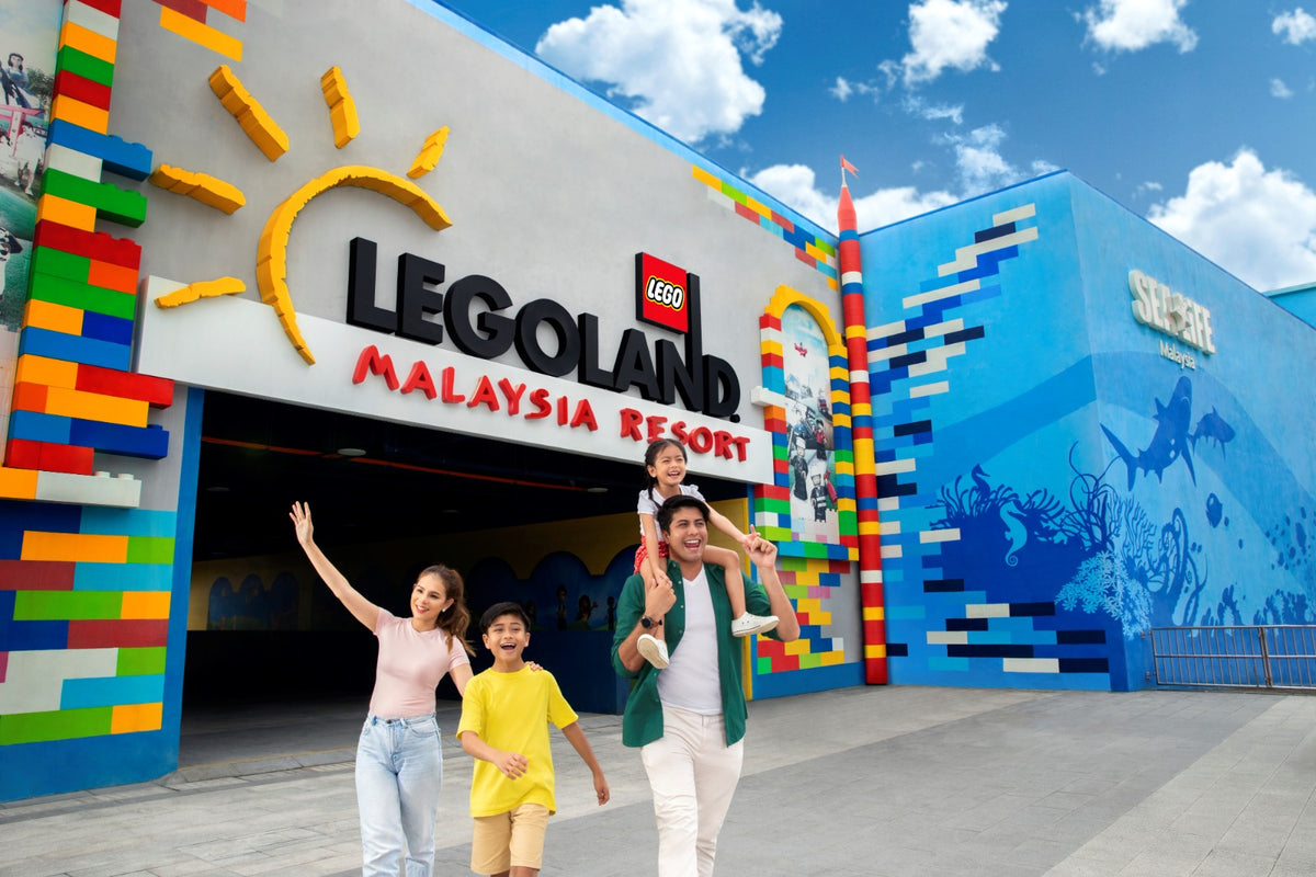 A family walking out from the LEGOLAND Malaysia Resort entrance, with the blue SEA LIFE shark mural on the wall to the right.