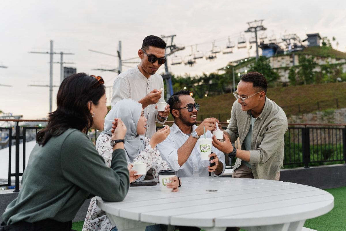 A group at an outdoor table with desserts, the luge track and chairlift on the hill behind.