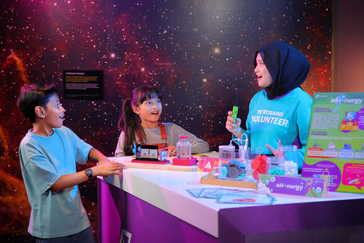 A Petrosains volunteer showing two children a hydrogen fuel cell experiment at the eH-nergy bench.