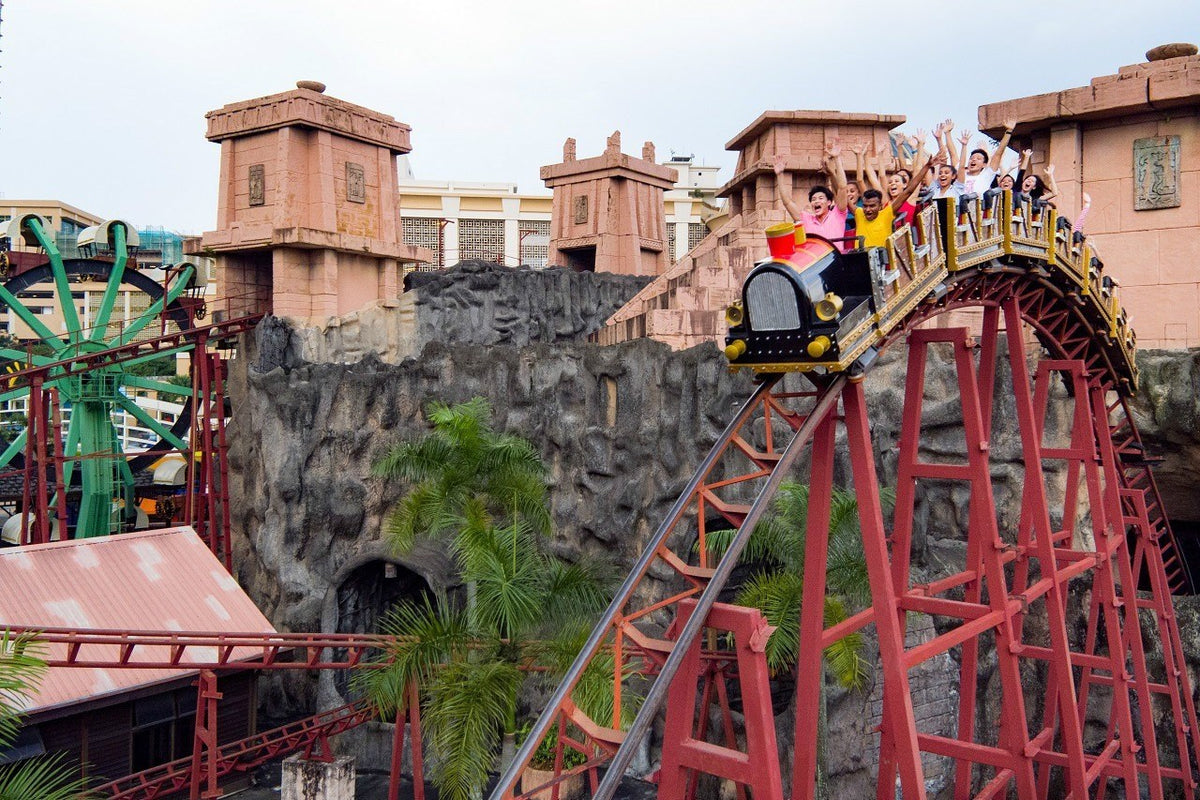 A roller coaster train cresting a hill above the park's stone-built theming.
