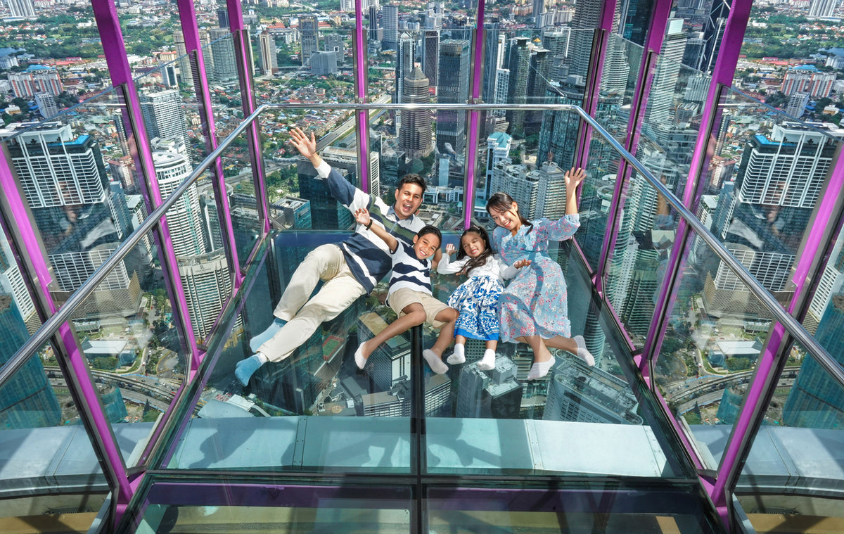 Looking down through the Sky Box glass floor at the city, with a family lying on it.