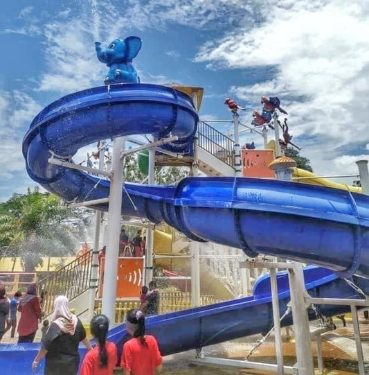 A blue spiral waterslide topped with an elephant sculpture, visitors watching from below.