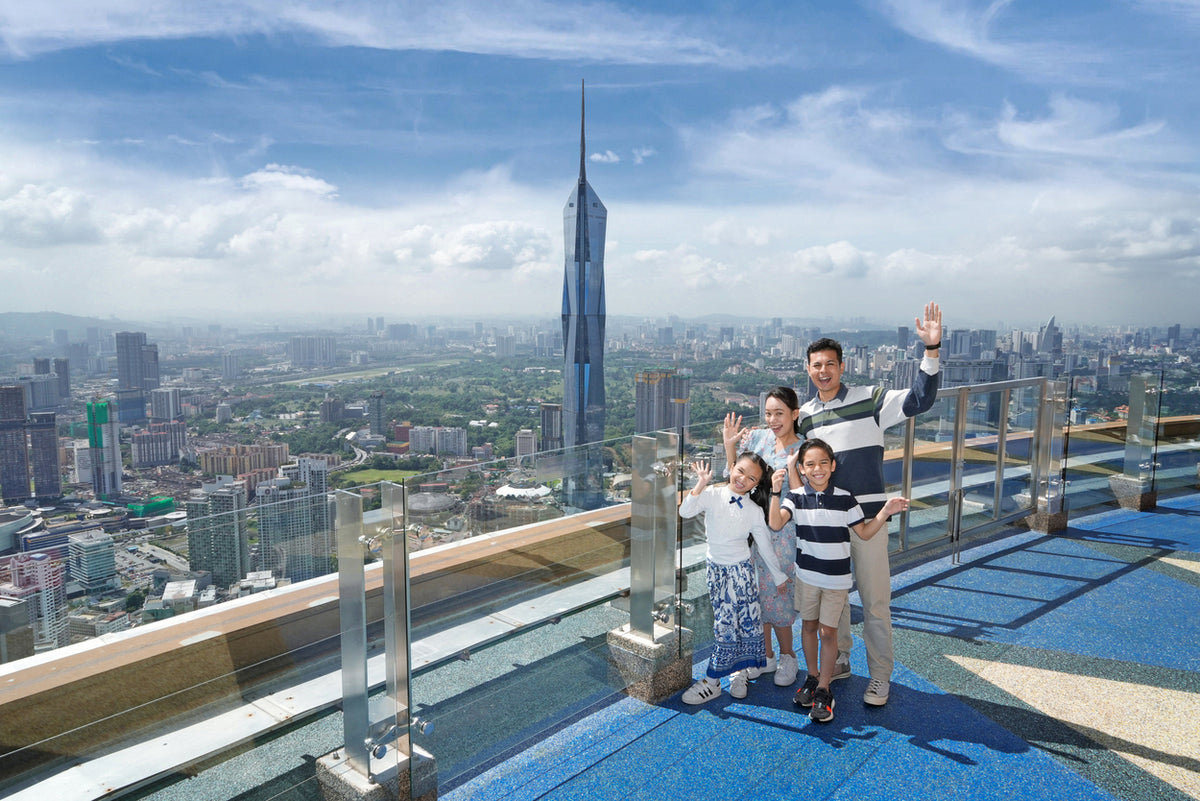 Visitors waving on the blue-floored Sky Deck with Kuala Lumpur spread out below.