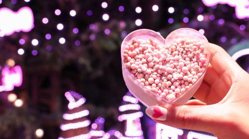 A heart-shaped dish of pink popcorn held up under the park lights