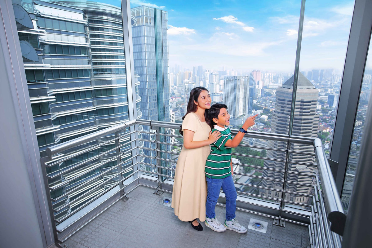 A woman and a boy on the Skybridge looking out over Kuala Lumpur, the boy pointing at something below.