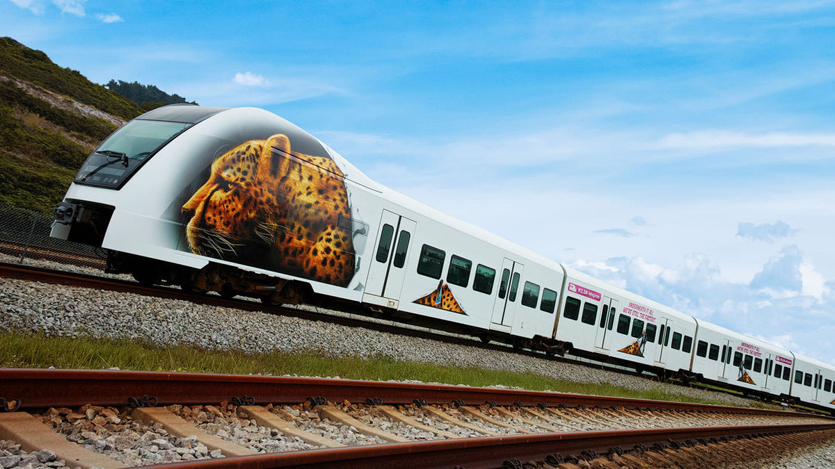 A KLIA Ekspres train with leopard nose artwork running along the line through open country.