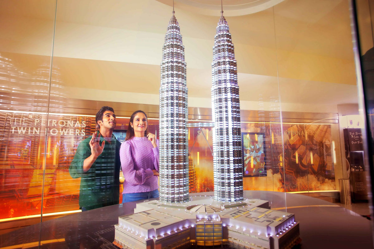 Two visitors looking up at the illuminated scale model of the PETRONAS Twin Towers in the exhibition gallery.