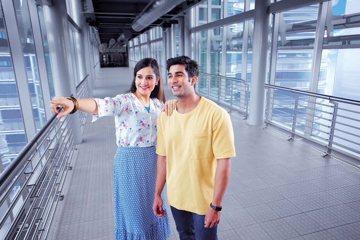 A couple on the Skybridge, one of them pointing out something through the glass.