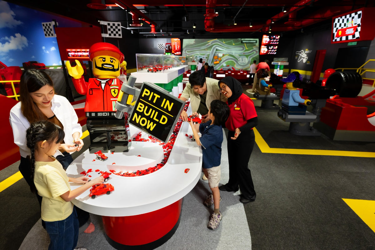 A family and a member of staff at the Ferrari Build and Race build station, with a giant LEGO Ferrari pit-crew minifigure behind.
