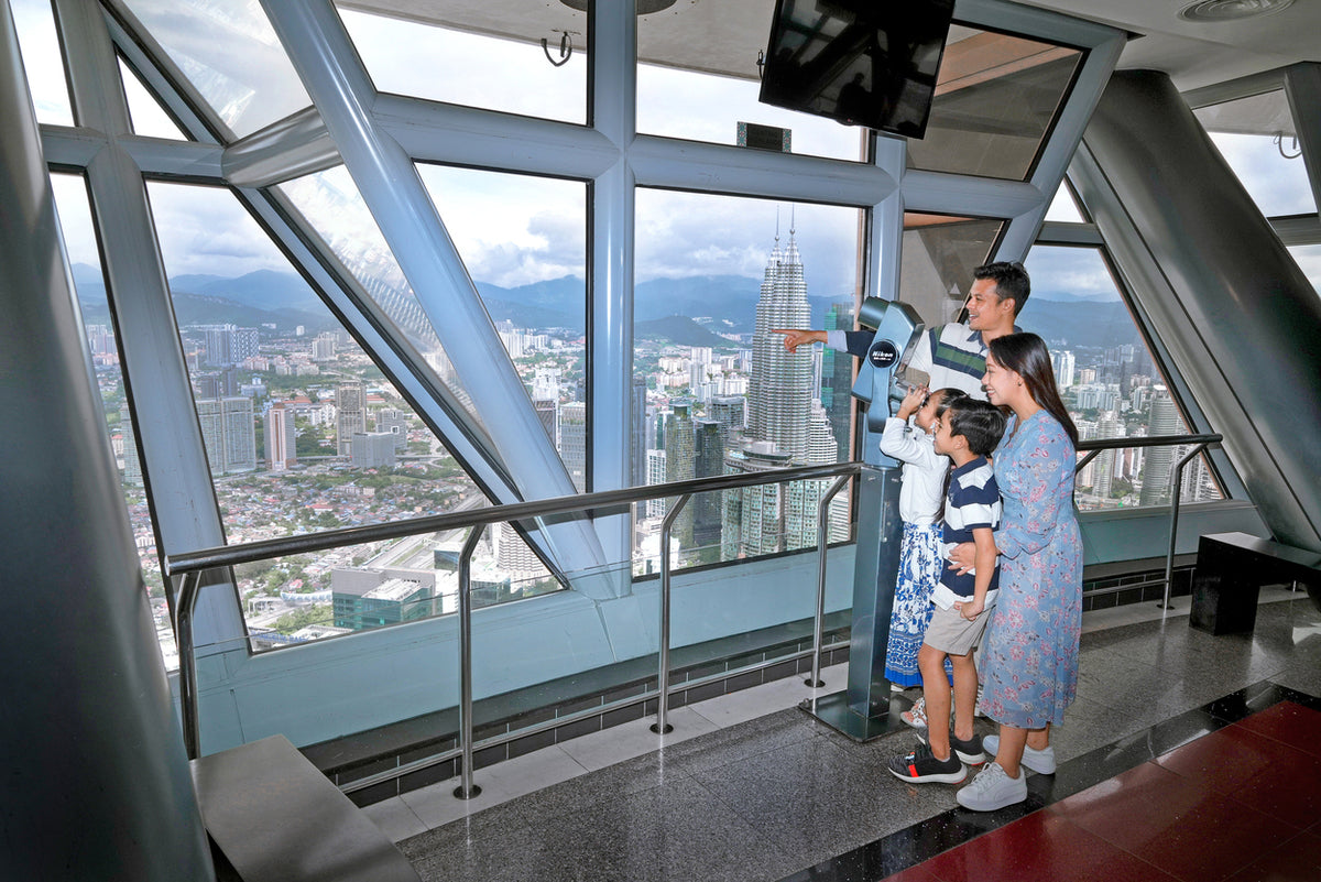 A family at the observation deck windows using a viewing telescope over the city.