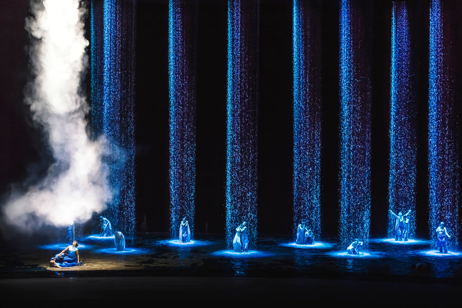 A lone boat on the flooded stage between tall blue curtains of falling water.