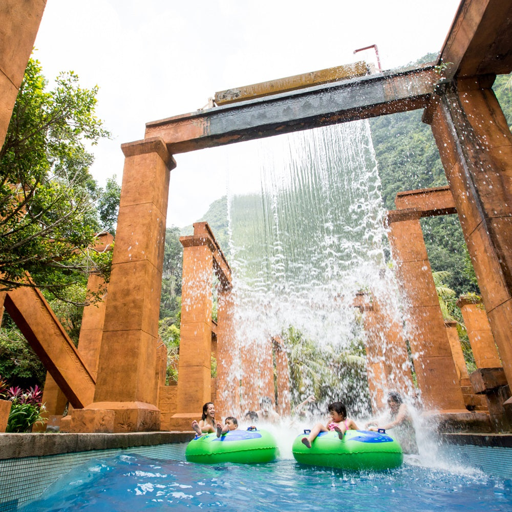 Visitors on rings passing under a waterfall between tall stone pillars.