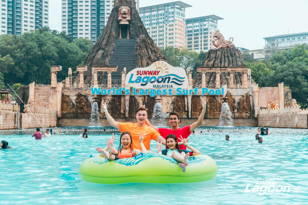 Visitors riding a green ring in the Sunway Lagoon surf pool beneath the volcano structure.