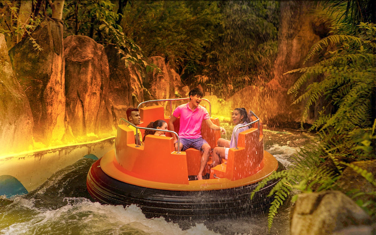 Riders in a round raft on the rapids ride, lit orange by the surrounding theming.