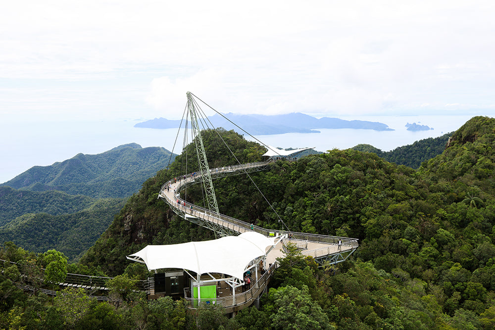 The curved Langkawi SkyBridge suspended above forested ridges, with islands beyond.
