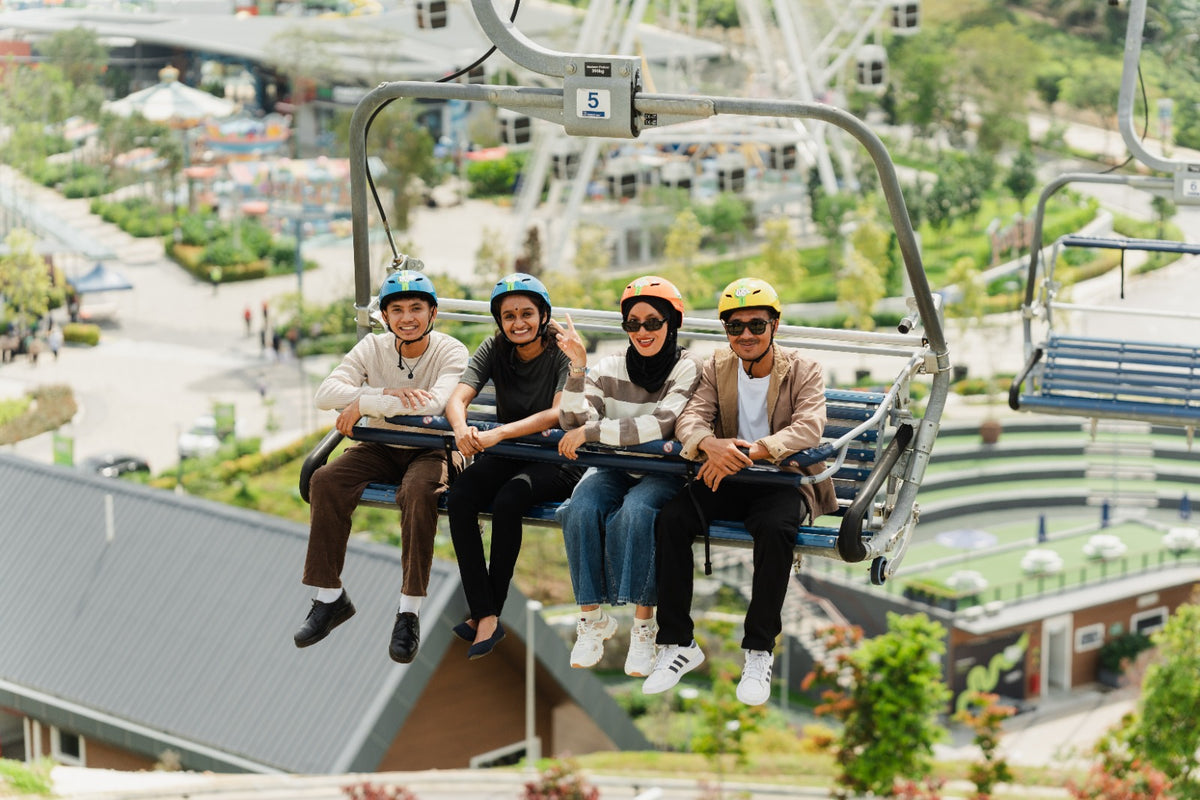 Four riders seated on the Skyride chairlift above the gardens and buildings below.