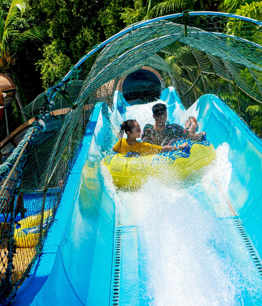 Two riders on a yellow tube rushing down a blue slide under a net canopy.