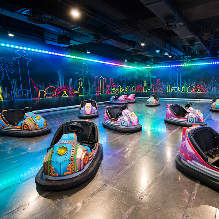 Empty dodgem cars waiting on a neon-lit indoor track.