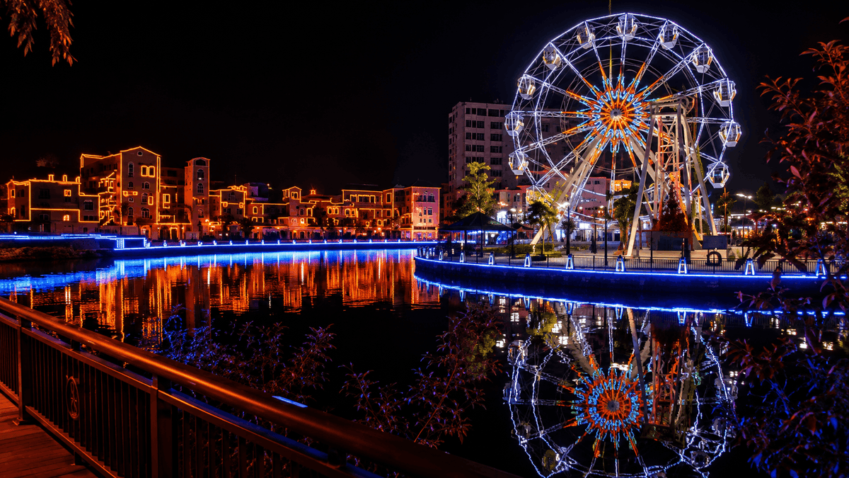 The Melaka waterfront at night, buildings and a Ferris wheel outlined in blue and orange light.